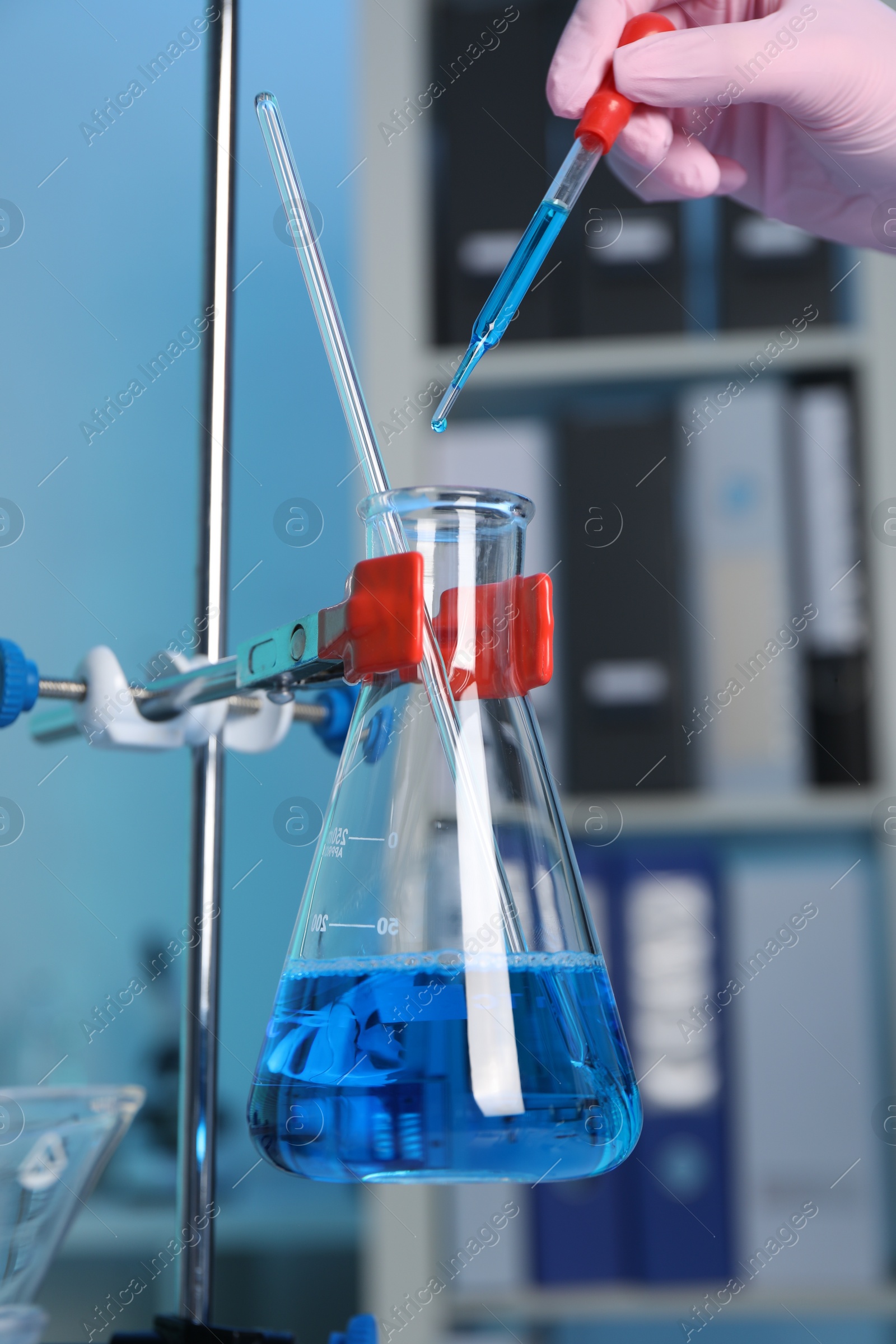 Photo of Laboratory analysis. Woman dripping blue liquid into flask on stand indoors, closeup