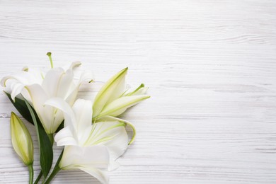 Photo of Beautiful lily flowers on white wooden table, flat lay. Space for text