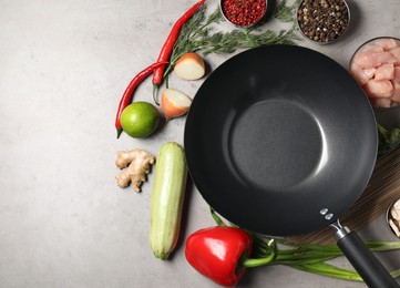 Empty iron wok surrounded by raw ingredients on grey table, flat lay. Space for text