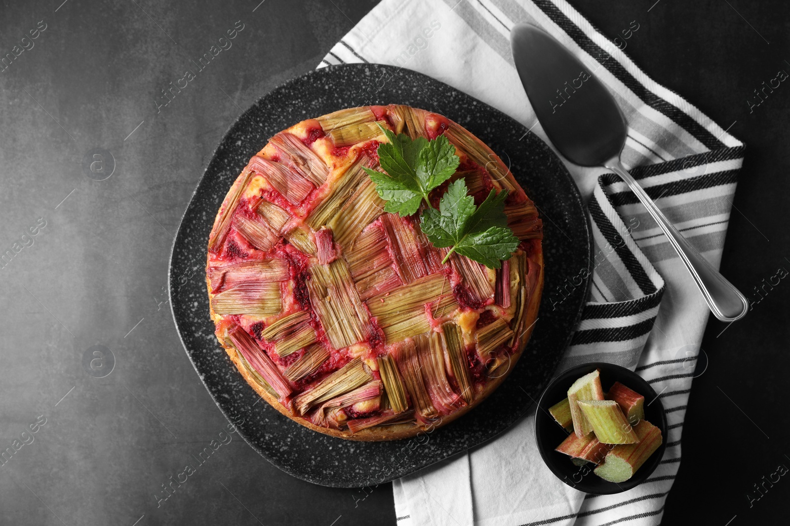 Photo of Freshly baked rhubarb pie, cut stalks and cake server on black table, flat lay