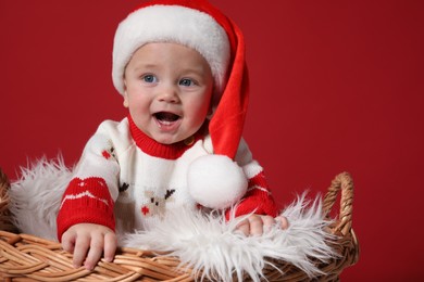 Photo of Cute baby in wicker basket on red background. Christmas celebration