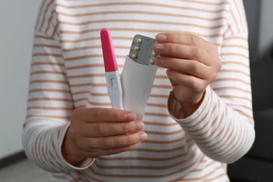 Woman holding birth control pills pregnancy test indoors, closeup