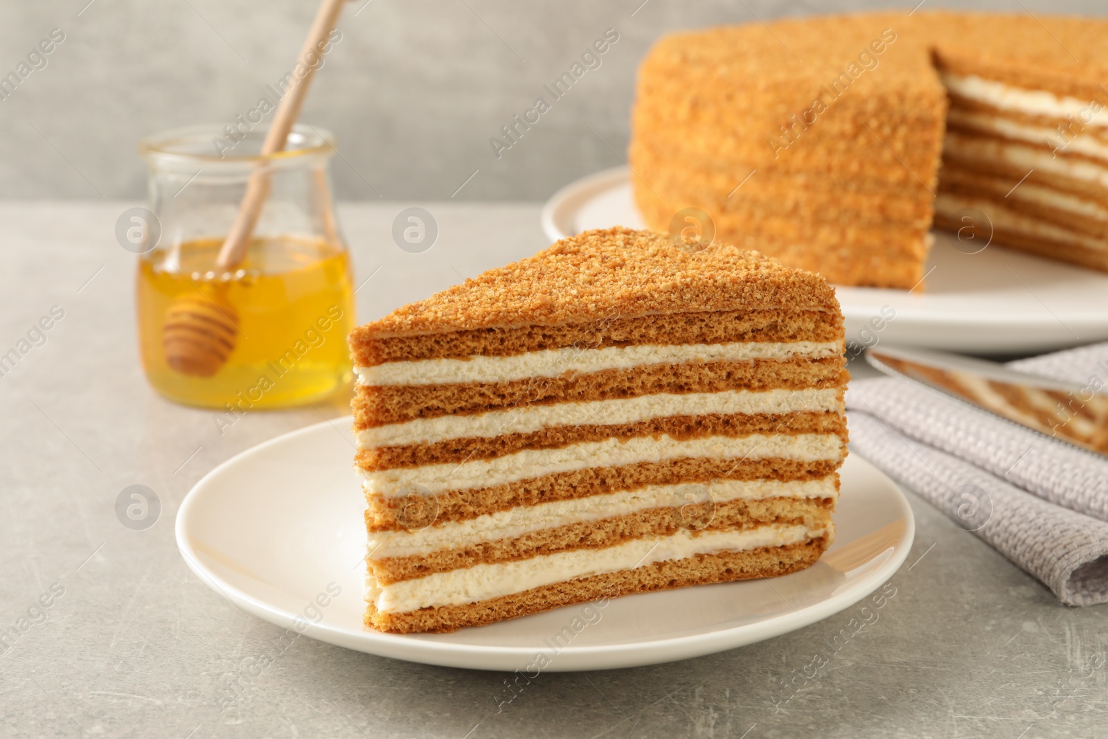 Photo of Slice of delicious layered honey cake served on grey table, closeup