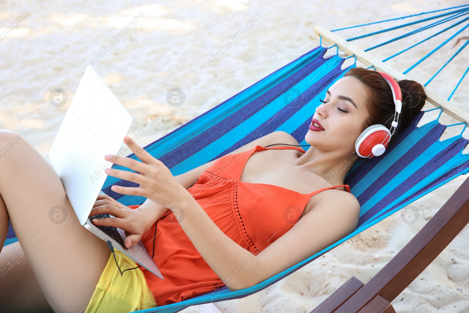 Photo of Young woman listening to music in comfortable hammock at seaside