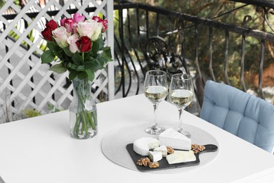 Beautiful roses, glasses of wine and snacks on white table at balcony