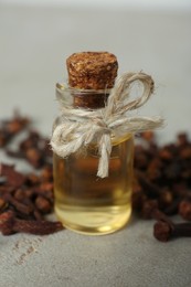 Essential oil and dried cloves on light grey table, closeup