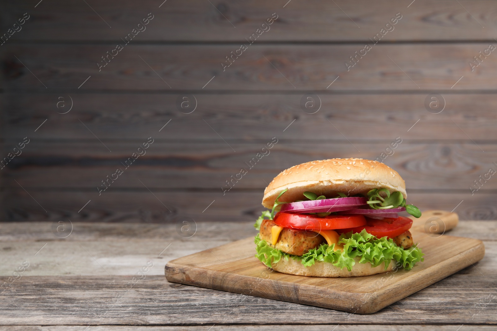 Photo of Delicious burger with tofu and fresh vegetables on wooden table. Space for text