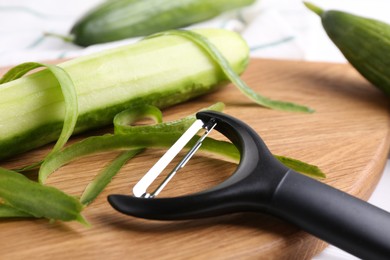 Photo of Fresh cucumbers, peels and peeler on white table, closeup
