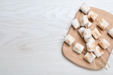 Photo of Sticks with roasted marshmallows on white wooden table, top view. Space for text