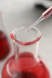 Photo of Laboratory analysis. Dripping red liquid into flask at light grey table, closeup