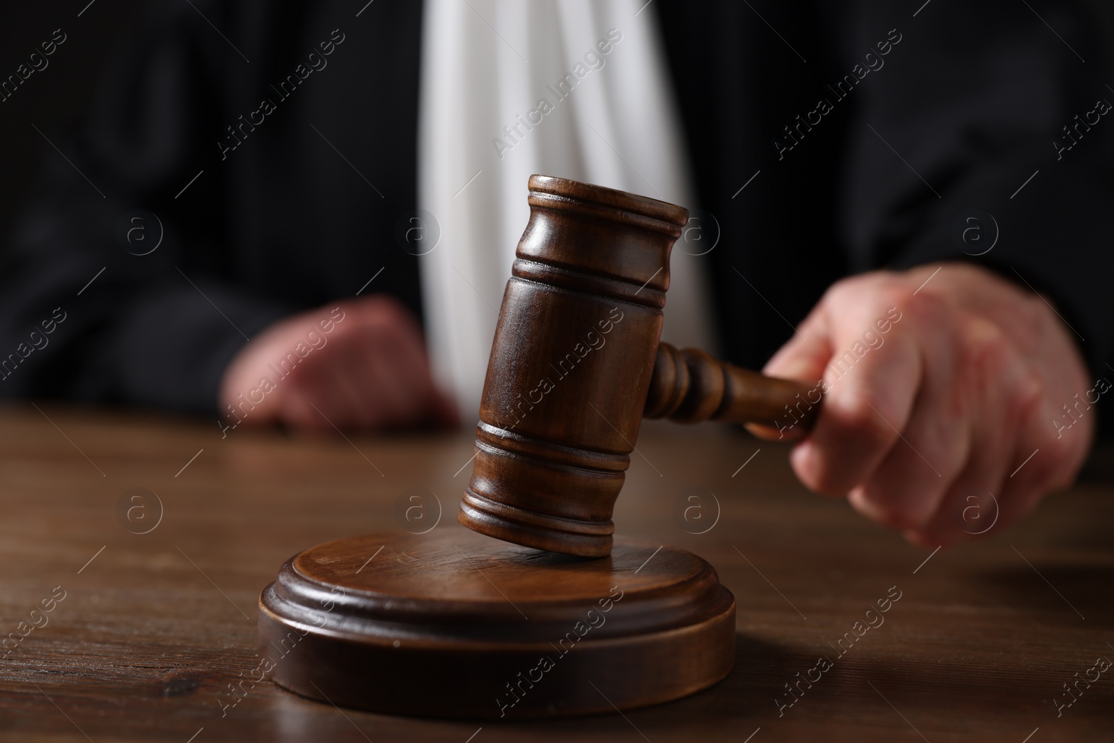 Photo of Judge with gavel sitting at wooden table against black background, closeup