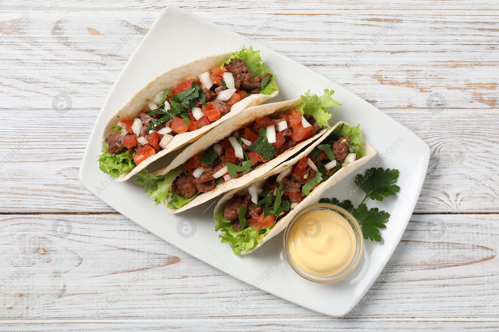 Photo of Delicious tacos with meat and vegetables served on wooden table, top view