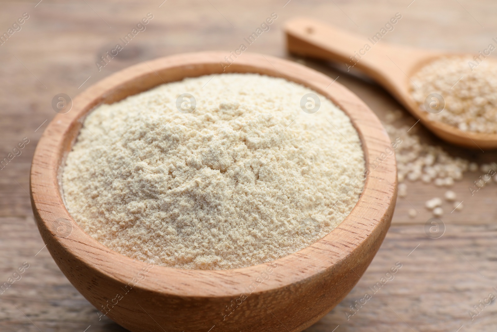 Photo of Quinoa flour in bowl and spoon with seeds on wooden table, closeup