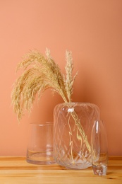 Vase with spikelets and decoration on wooden table near brown wall. Interior design