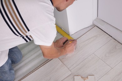 Photo of Man using measuring tape during installation of laminate flooring, closeup