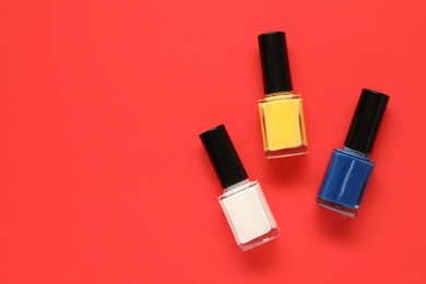 Photo of Bright nail polishes in bottles on red background, flat lay. Space for text