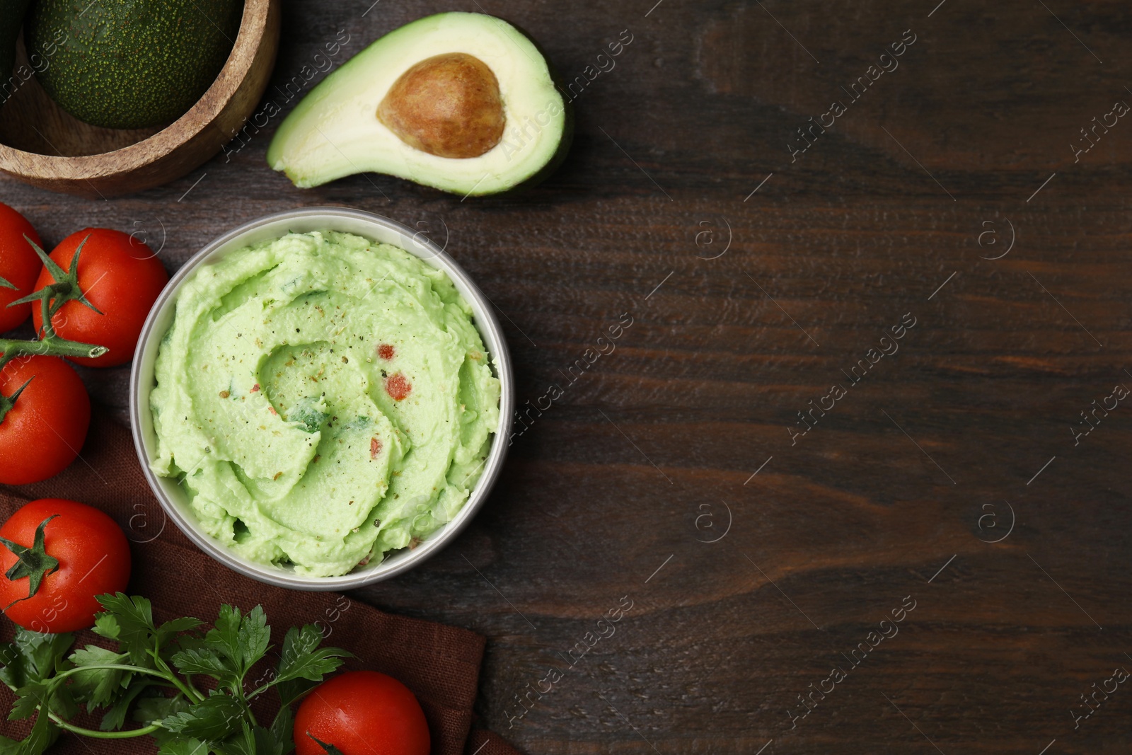 Photo of Bowl of delicious guacamole and ingredients on wooden table, flat lay. Space for text