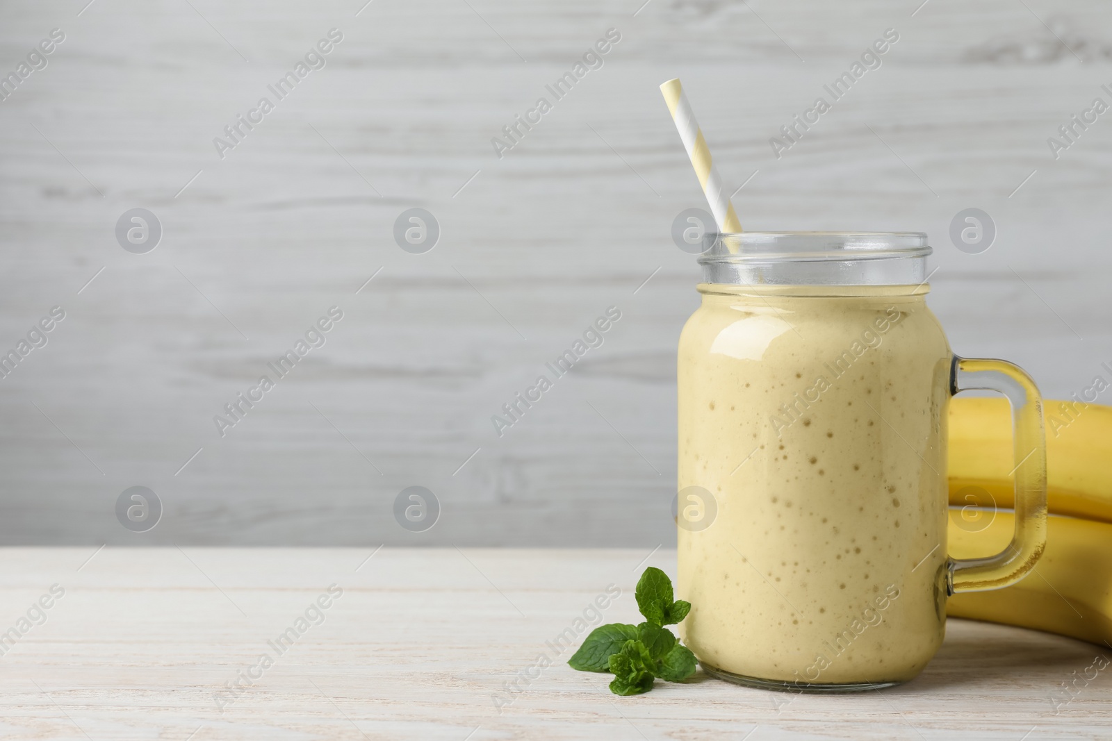 Photo of Mason jar with delicious fruit smoothie and fresh bananas on white wooden table. Space for text