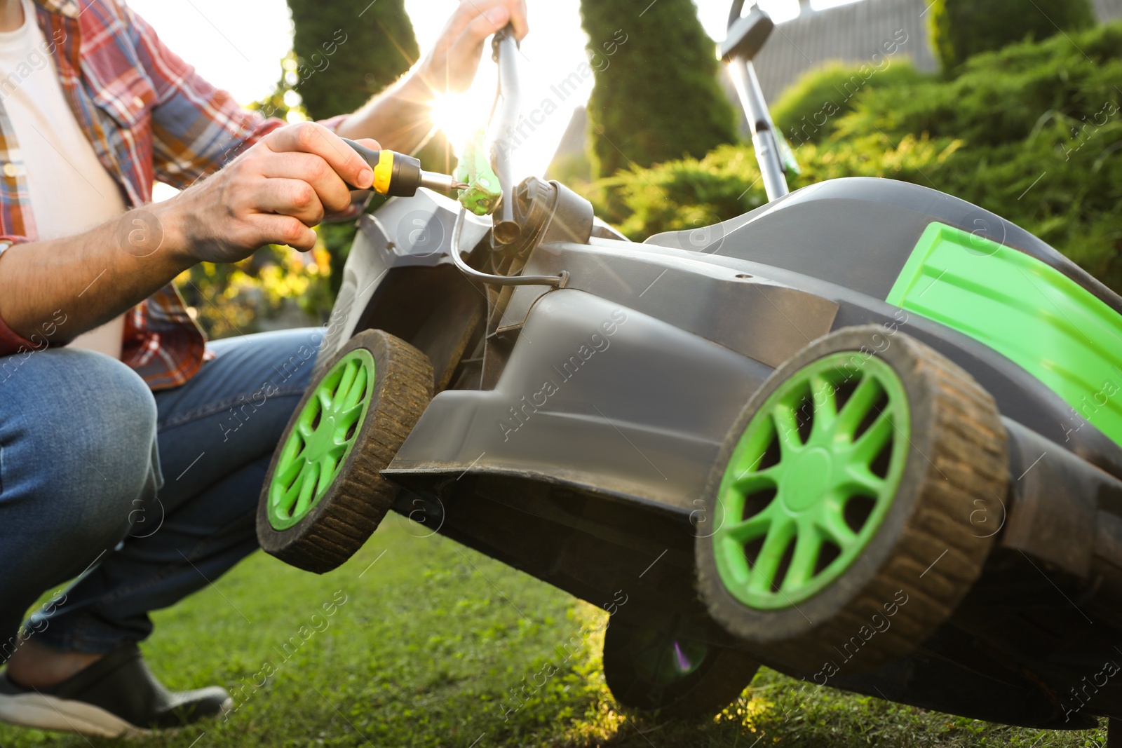 Photo of Man with screwdriver fixing lawn mower in garden, closeup