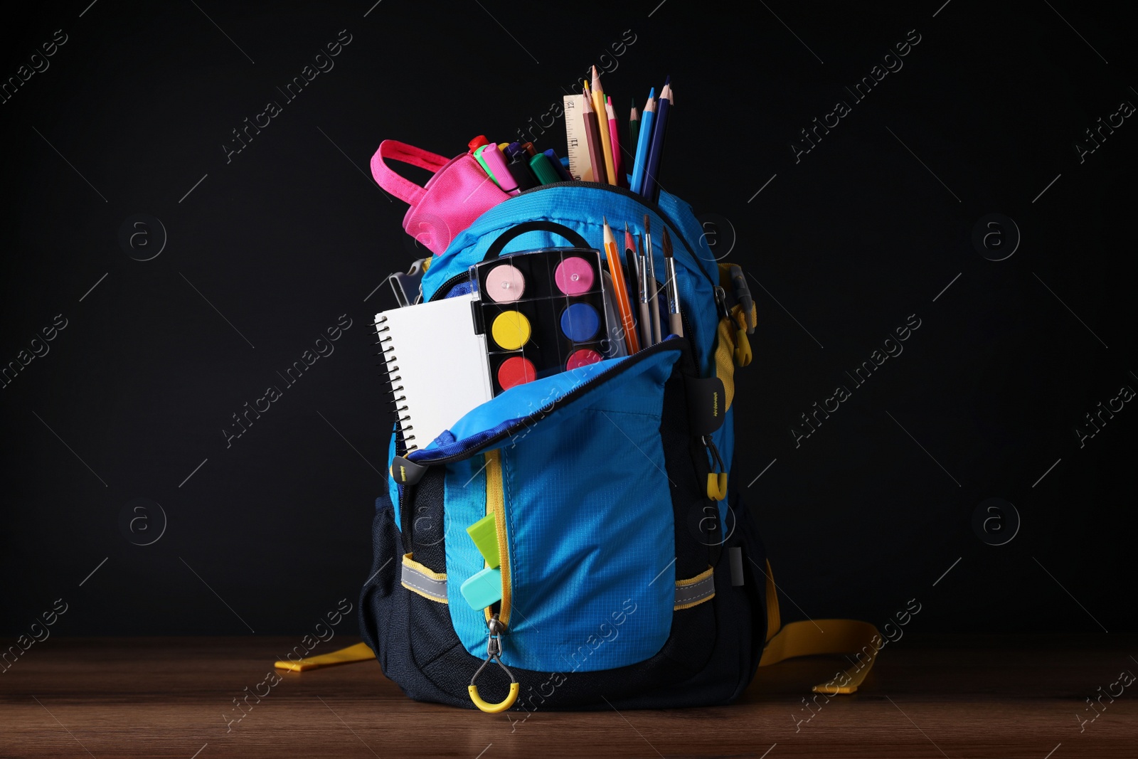 Photo of Backpack with different school stationery on wooden table near blackboard