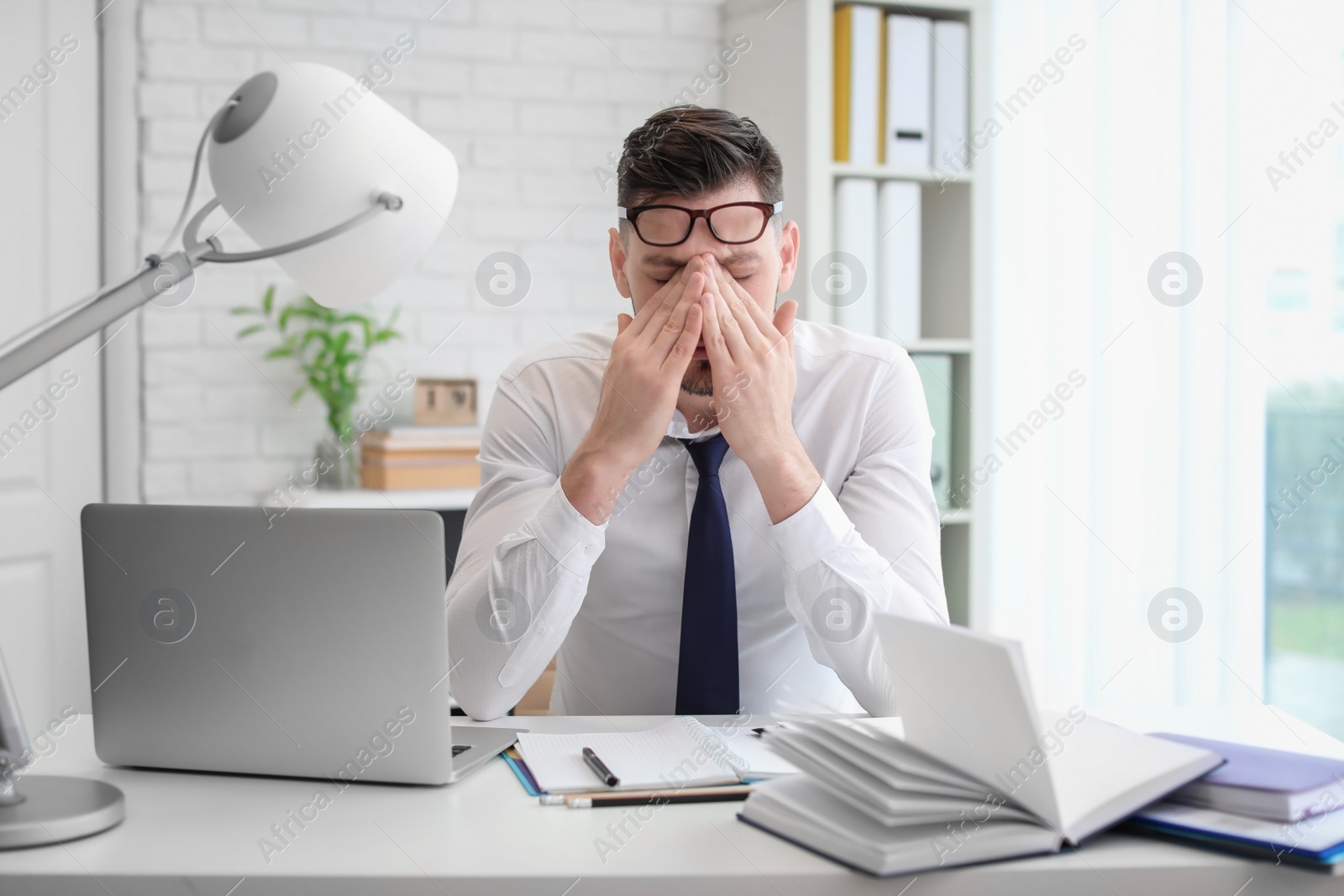 Photo of Man suffering from headache while sitting at table in office