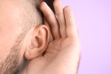 Photo of Young man with hearing problem on color background, closeup