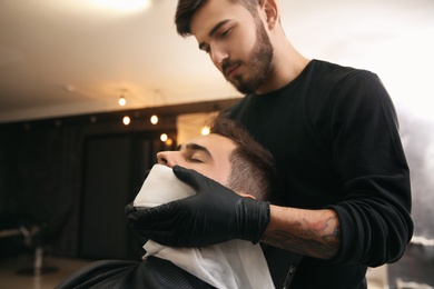 Photo of Professional hairdresser using cold towel to calm client's skin after shaving in barbershop
