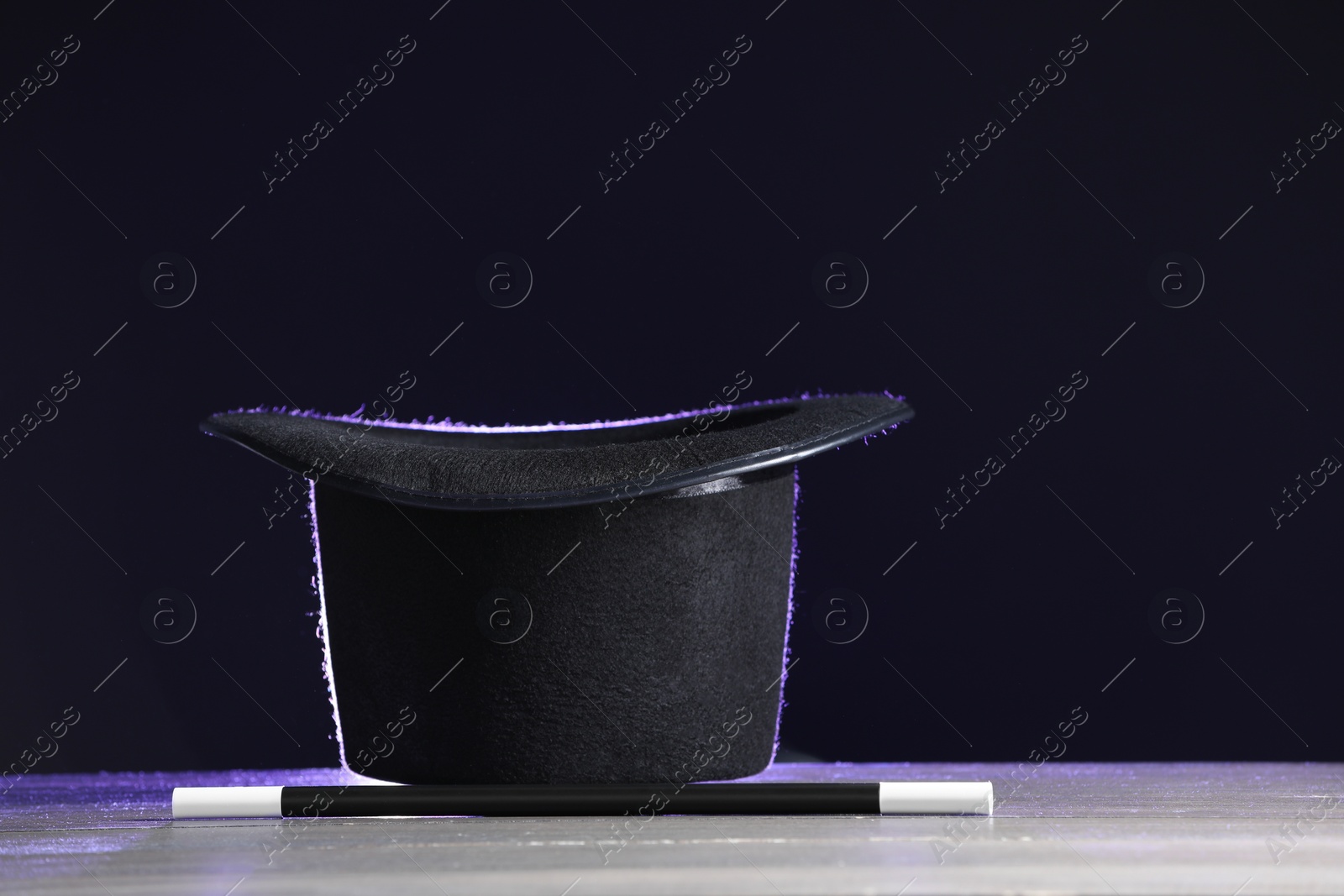 Photo of Magician's hat and wand on white wooden table against black background