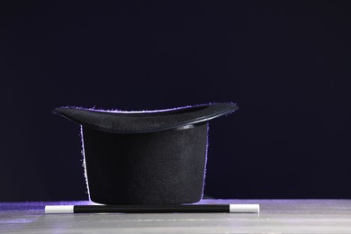 Photo of Magician's hat and wand on white wooden table against black background