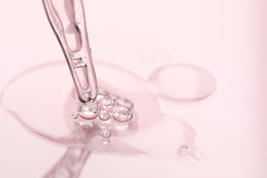 Glass pipette and transparent liquid on light pink background, closeup. Space for text