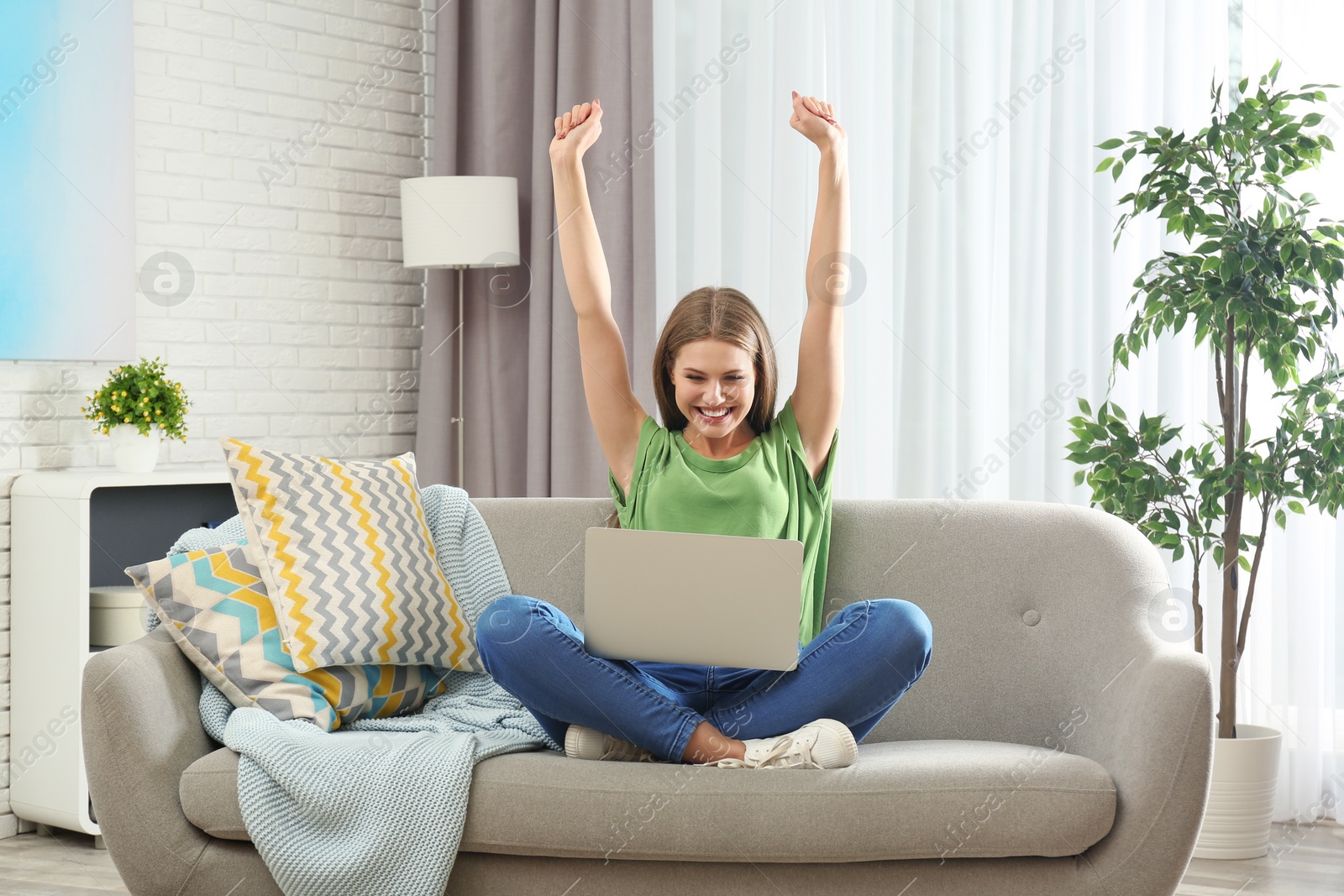 Photo of Emotional young woman with laptop celebrating victory on sofa at home