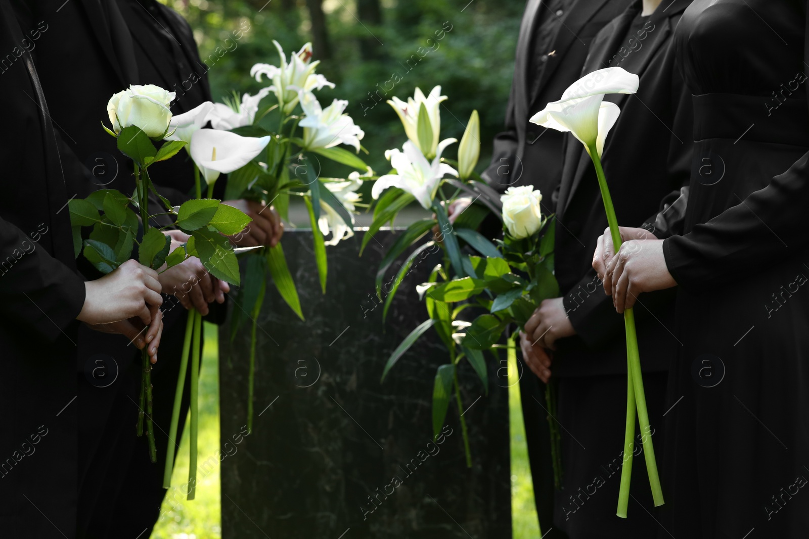 Photo of People with flowers near granite tombstone at cemetery outdoors, closeup. Funeral ceremony