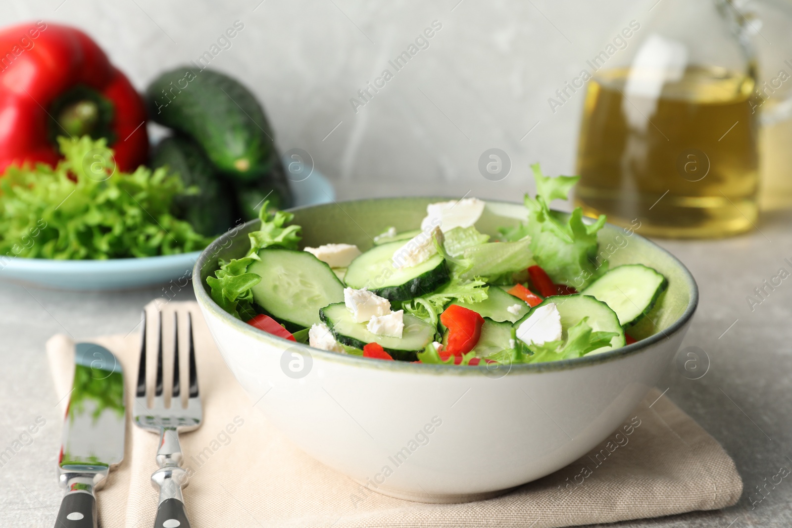 Photo of Delicious salad with cucumbers, red bell pepper and feta cheese in bowl served on light grey table