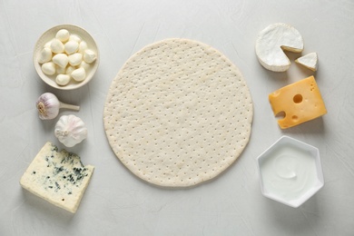 Flat lay composition with pizza crust and fresh ingredients on white table