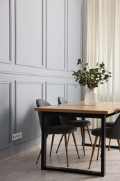 Photo of Soft chairs, table and vase with eucalyptus branches in stylish dining room