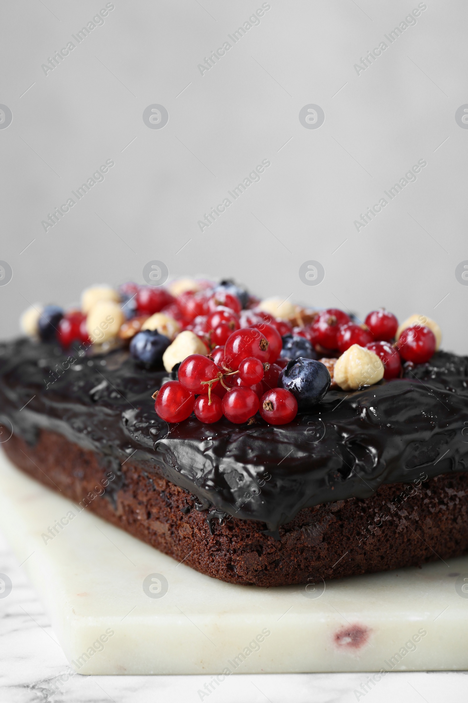 Photo of Delicious chocolate sponge cake with berries and nuts on white table, closeup