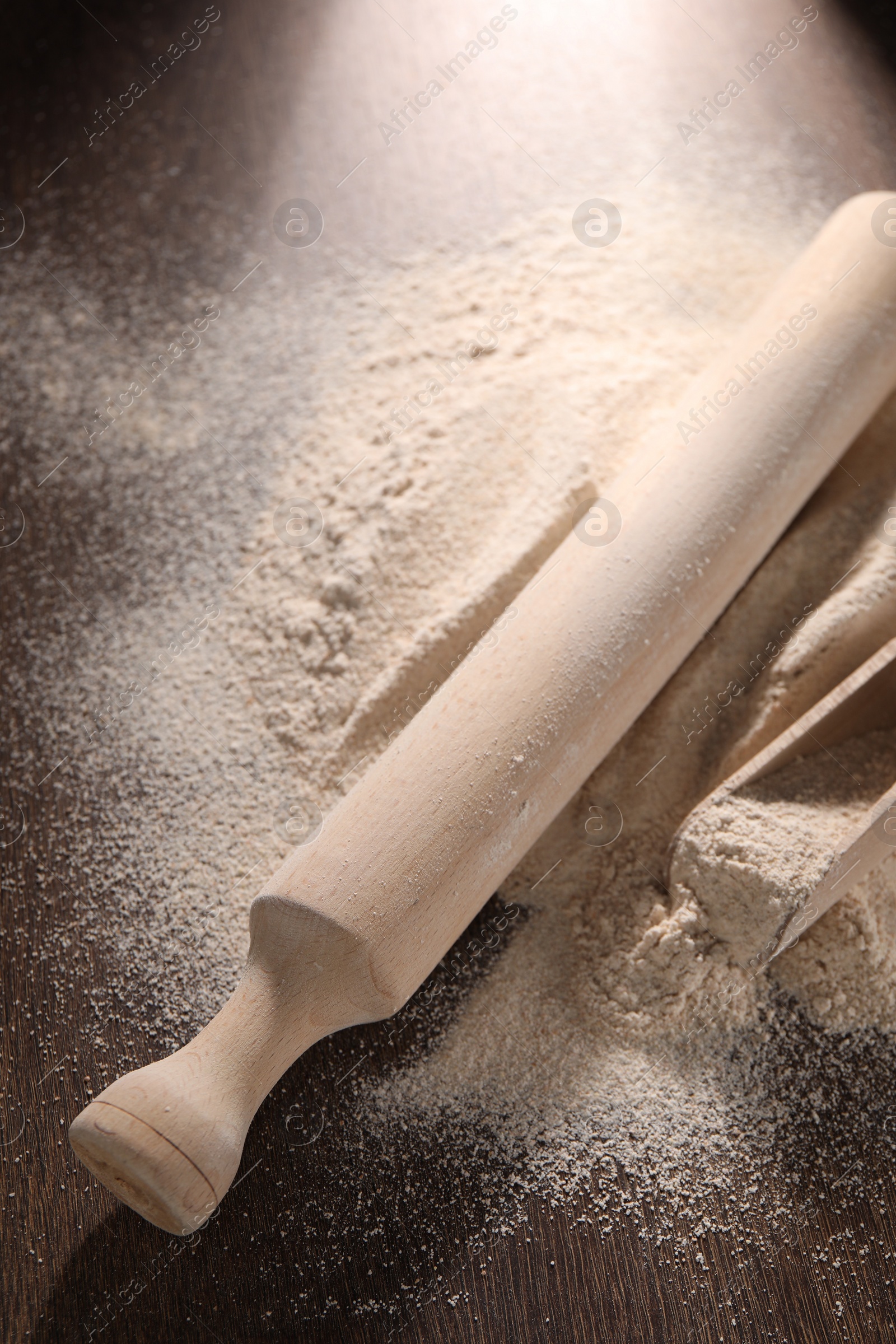 Photo of Pile of flour, rolling pin and scoop on wooden table, closeup