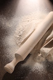 Pile of flour, rolling pin and scoop on wooden table, closeup