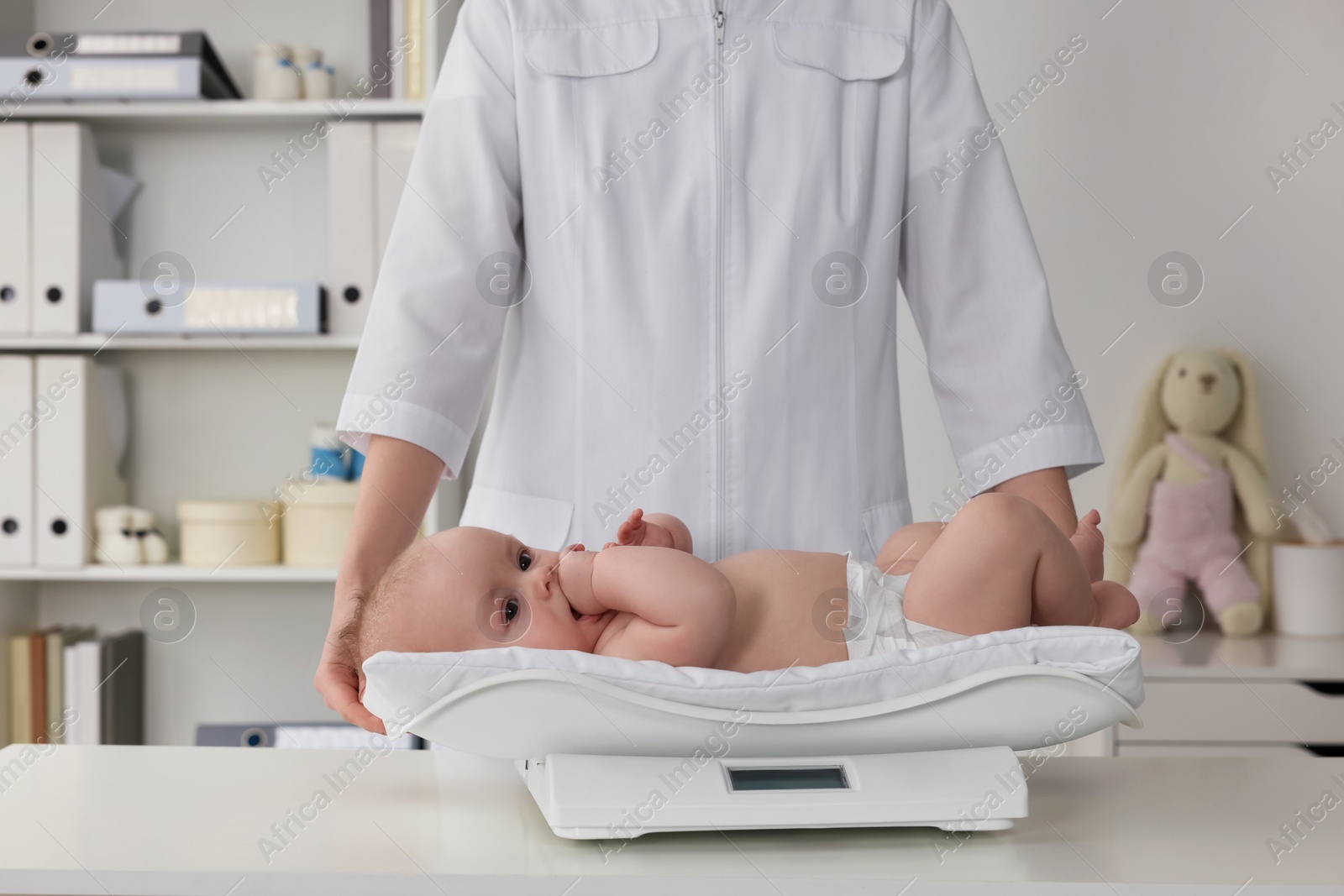 Photo of Pediatrician weighting cute little baby in clinic, closeup