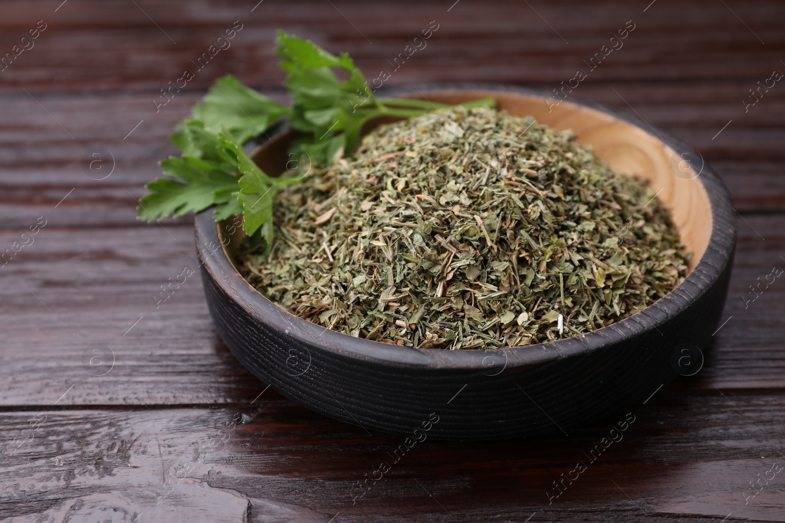 Photo of Dried aromatic parsley and fresh leaves in plate on wooden table, closeup