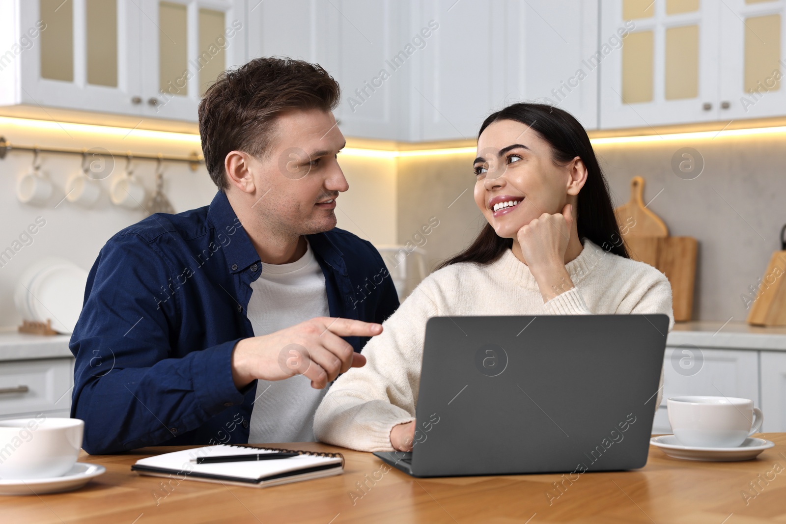 Photo of Happy couple using laptop at wooden table in kitchen