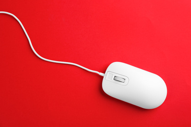 Modern wired optical mouse on red background, top view