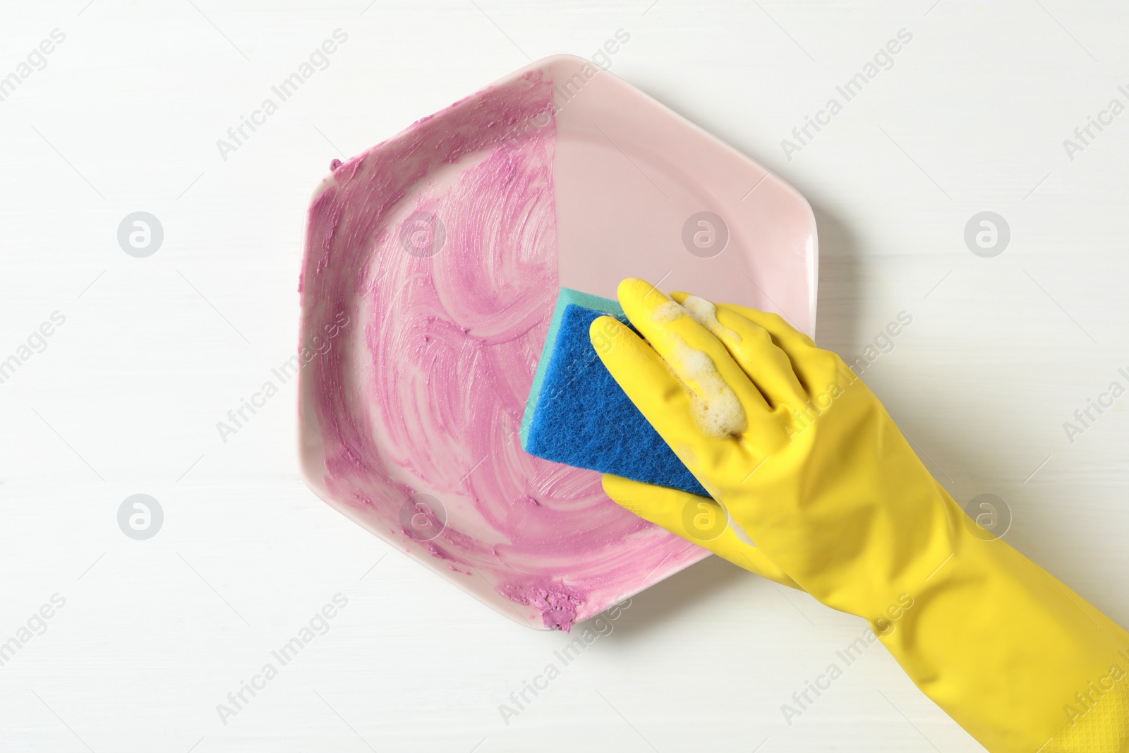 Photo of Woman washing dirty plate at white wooden table, top view