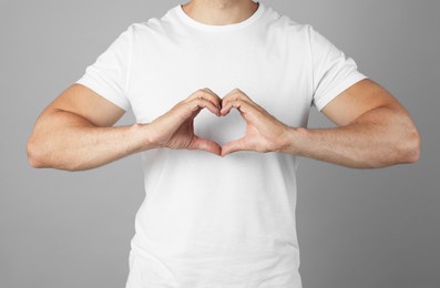 Photo of Man making heart with hands on grey background, closeup