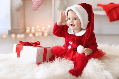 Photo of Cute baby in Christmas costume and gift box on floor at home