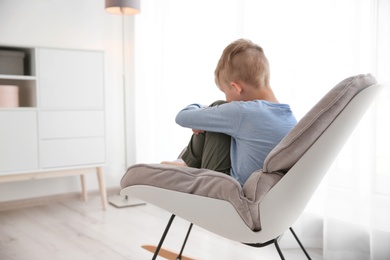 Lonely little boy sitting on chair at home. Autism concept