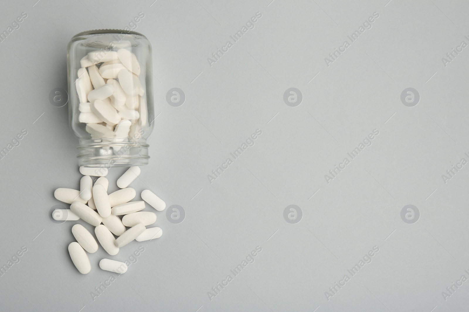 Photo of Vitamin pills and bottle on grey background, top view. Space for text