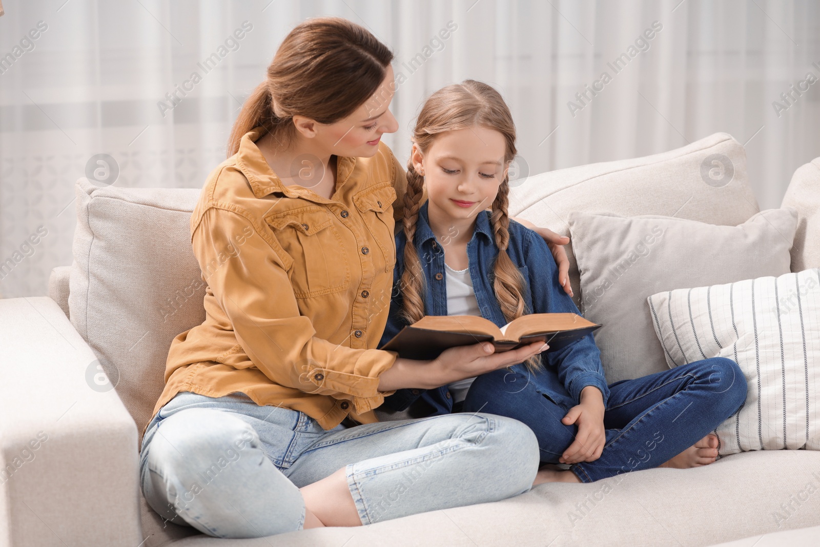 Photo of Girl and her godparent reading Bible together on sofa at home