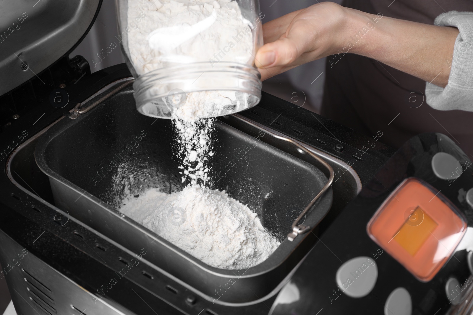 Photo of Woman adding flour into breadmaker indoors, closeup