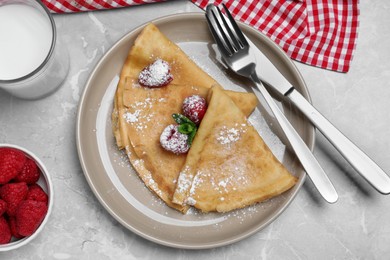 Photo of Delicious crepes served with mint, raspberries, powdered sugar and glass of milk on grey table, flat lay